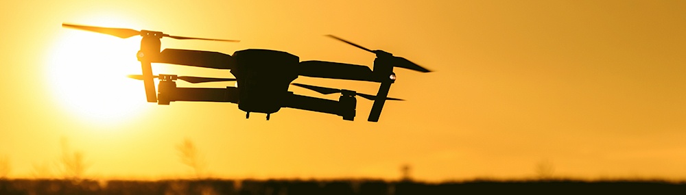 A close up of a drone flying with the sunset in the background.