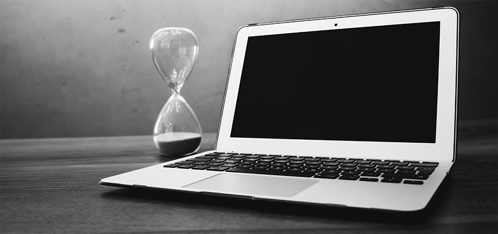 Laptop with hourglass on table.