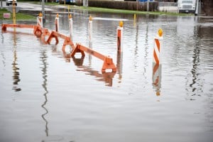Flooded transportation sign with road barriers on a cloudy day.