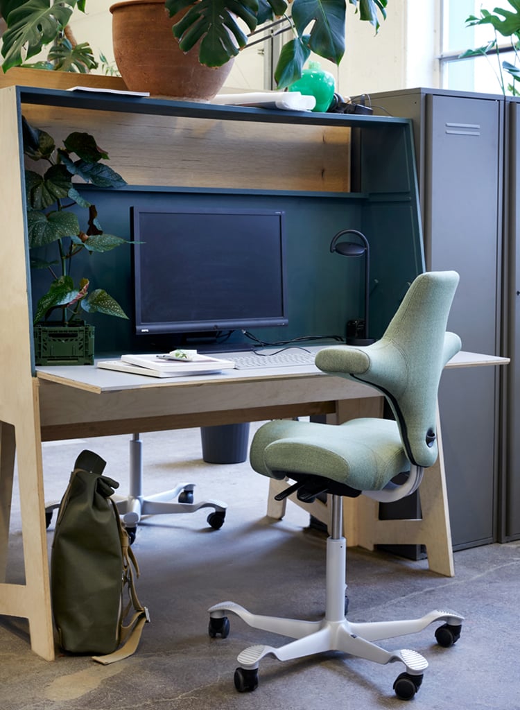 HÅG Capisco ergonomic chair in green fabric at a tidy workstation with computer and bag