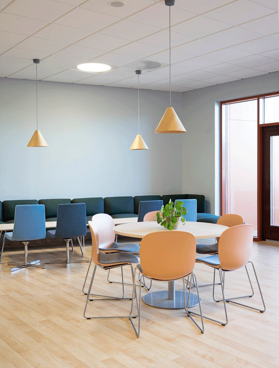 Clay coloured RBM Noor chairs arranged around a round table with pendant lighting in a cafe at Hebekk School, Norway