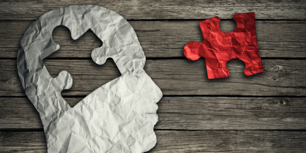 Puzzle head brain concept as a human face profile made from crumpled white paper with a jigsaw piece cut out on a rustic old wood background as a mental health symbol.