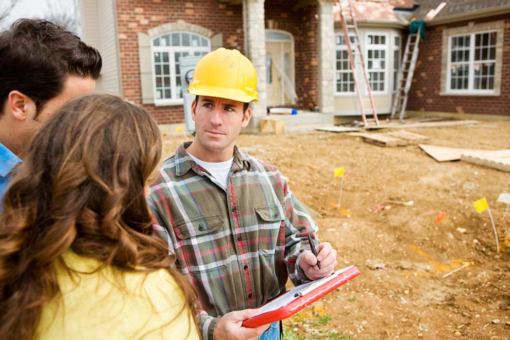 Contractor and a couple standing in front of a house being repaired