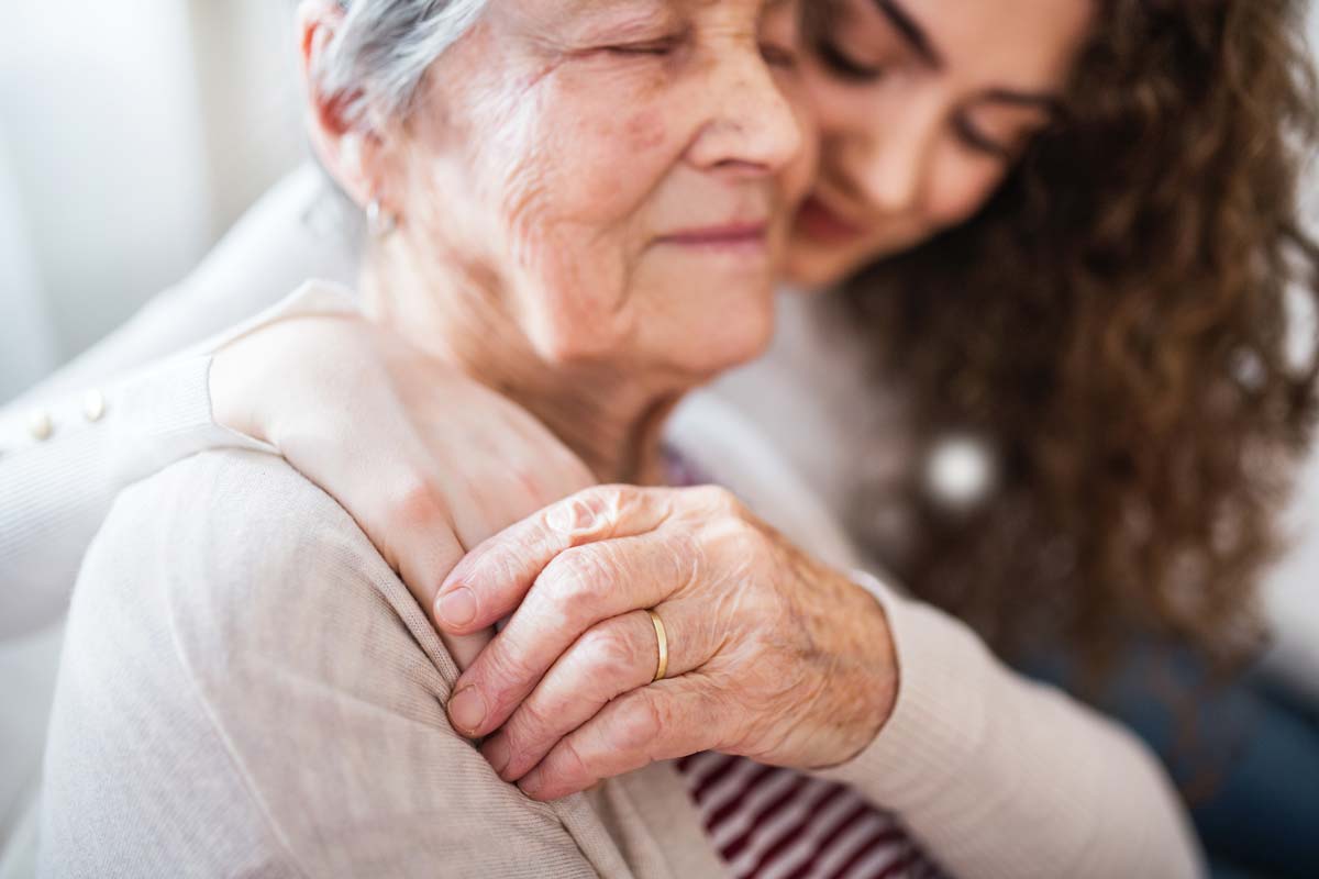 Woman embracing and older woman around her shoulder, holding hands