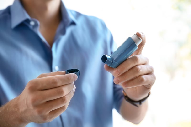 Man in blue shirt holding an inhaler.