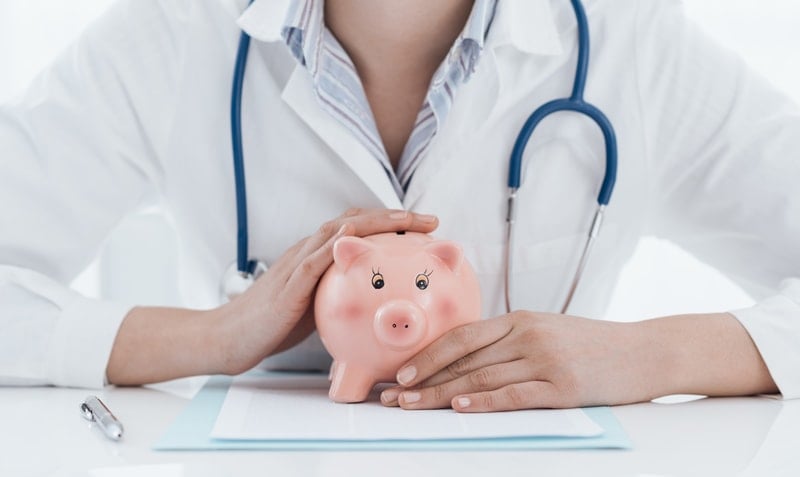 Doctor holding a piggy bank on a desk.
