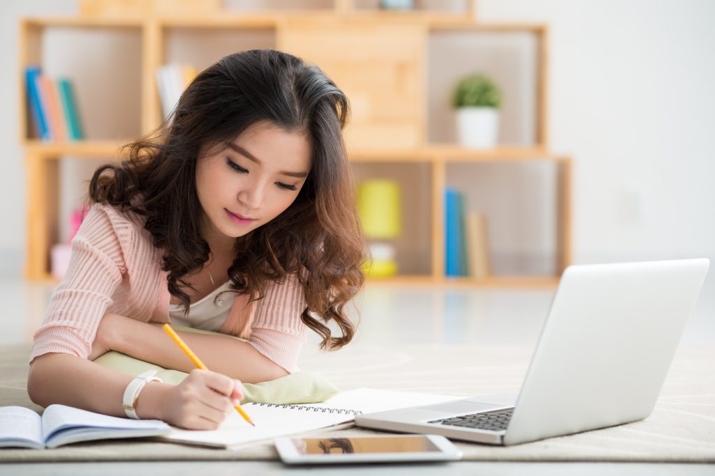 Pretty Asian girl working on her school project at home