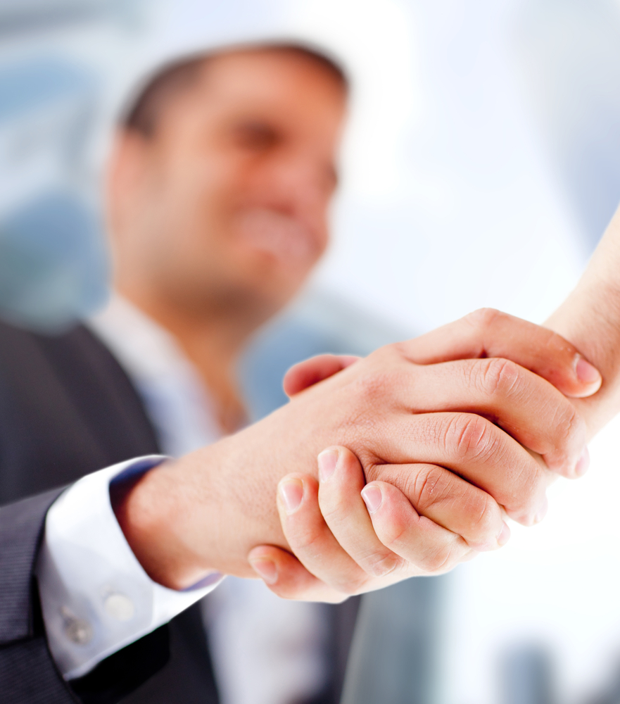 A business professional and a colleague are shaking hands. The focus is on the handshake, symbolizing a strong partnership and high employee engagement.
