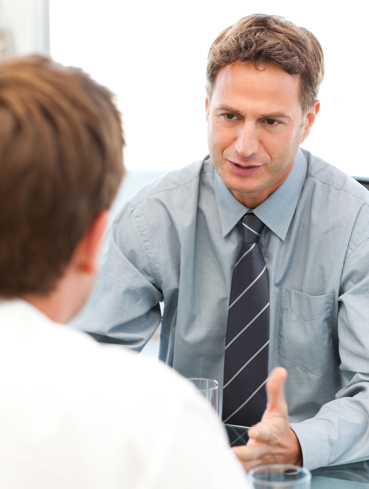 An in focus person in the background is wearing a tie is having a caring and concerned conversation with another person who is out of focus in the foreground.