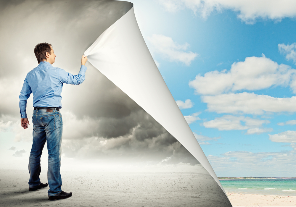 A man in jeans and a blue shirt pulls back a corner of a black & white picture of a beach to reveal a full color one behind representing the potential clarity of an organization using BITE7.