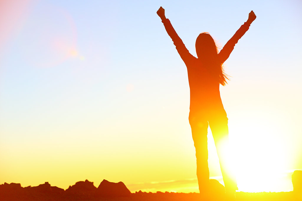 Employee engagement is key to success. A person with arms raised in victory at sunset captures the feeling of winning as a team.