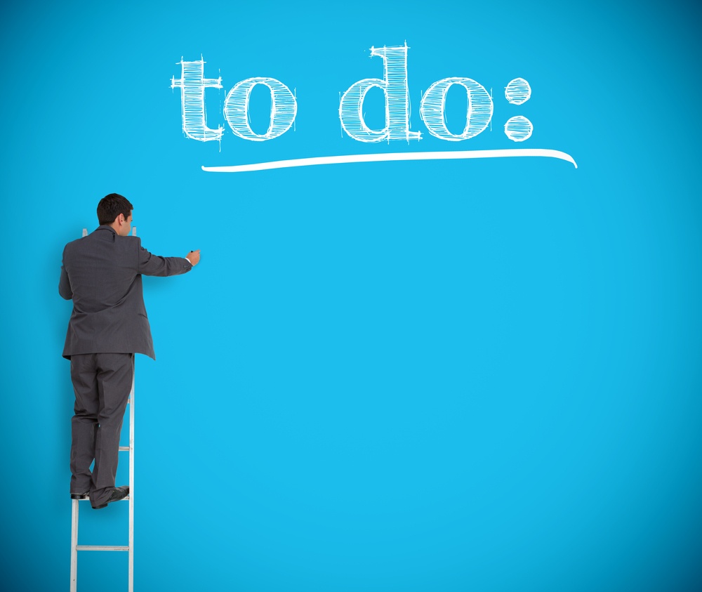 Businessman writing to do list on a giant blue wall helped by a ladder.jpeg