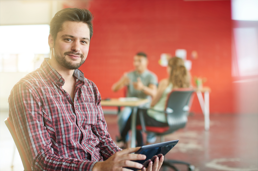 Confident male designer working on a digital tablet in red creative office space