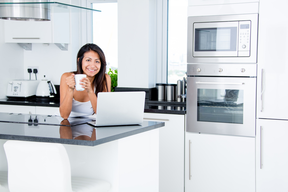 Happy woman in the kitchen reading he news on her laptop