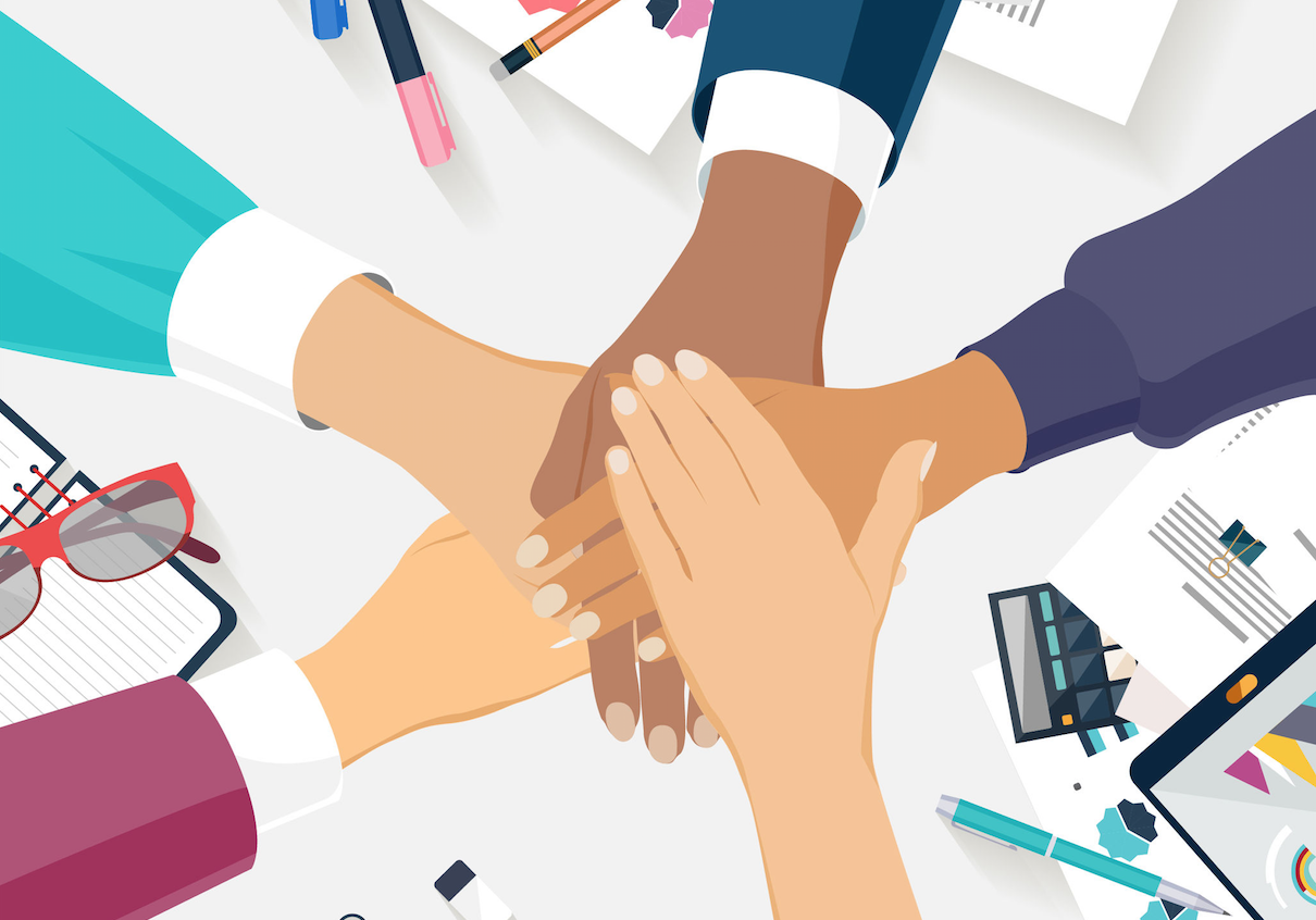 Five People's Hands Coming Together Above Desk with Office Items on It