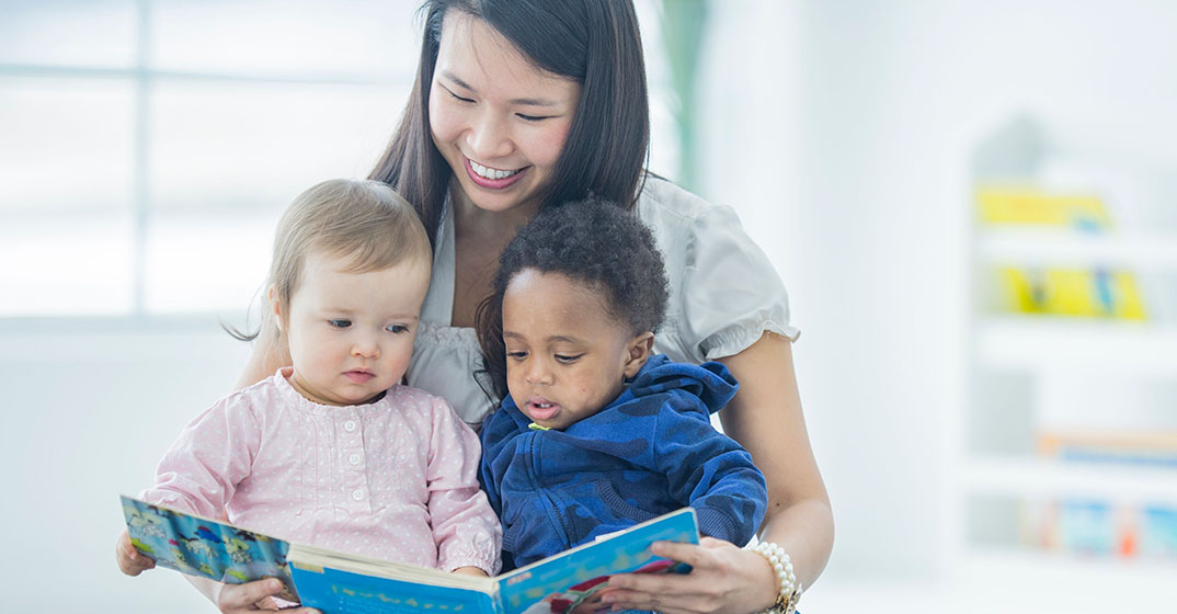 Provider reads a book to two toddlers.