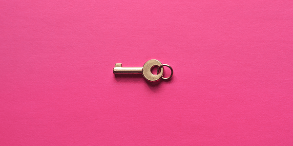 En nyckel i mässing mot rosa bakgrund 