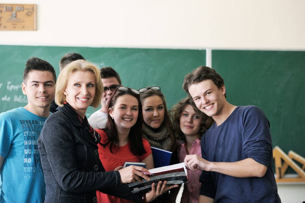 Teacher surrounded by her students in classroom holding a copybook