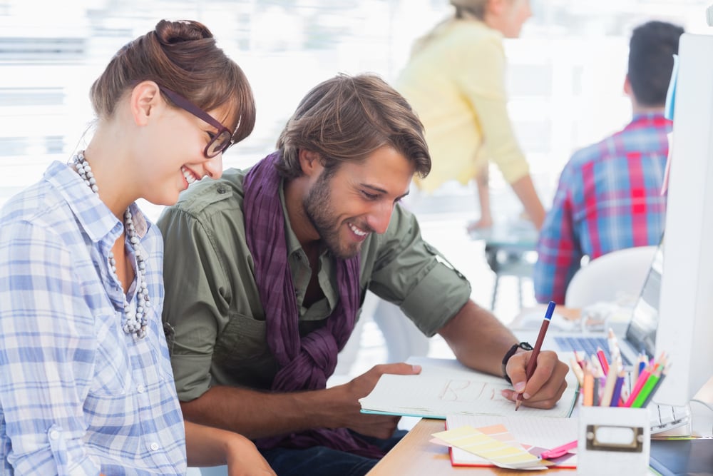 Happy designers working on a document with colleagues working behind-1