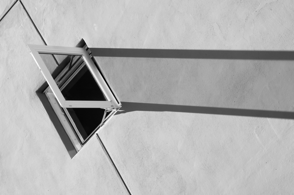 Open window and its long shadow on a sunlit wall