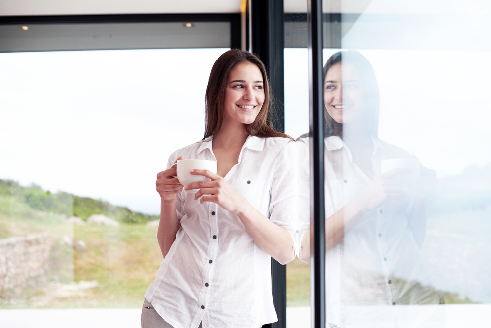 beautiful young woman drink first morning coffee at modern home interior with rain drops on big window door glass