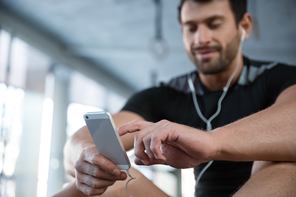 Portrait of a fitness man using smartphone in gym. Focus on smartphone
