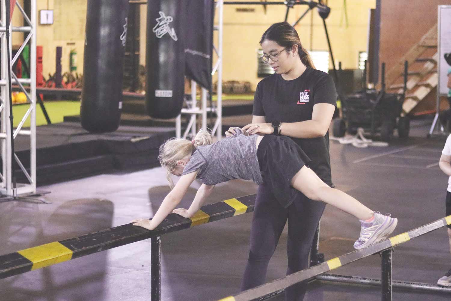 OCR Training TIps for Kids - Ladies Coach guiding girl through a parallel bar obstacle at PHO