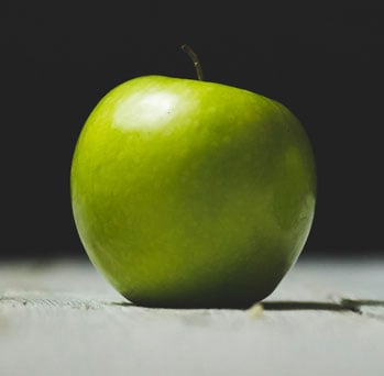 A green apple on a wooden surface with a dark background