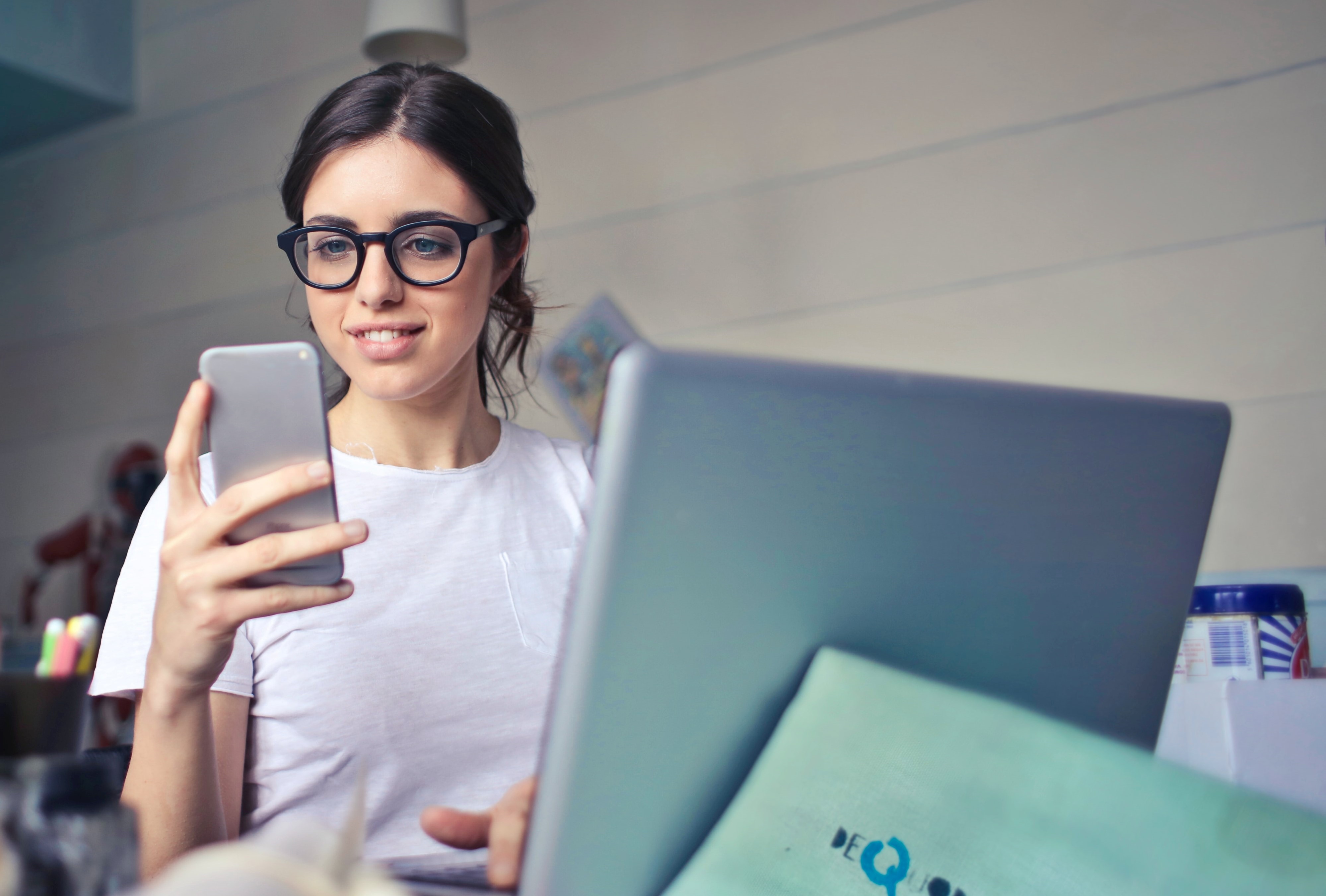 Kvinna som jobbar med försäljning sitter framför datorn och tittar i sin telefon