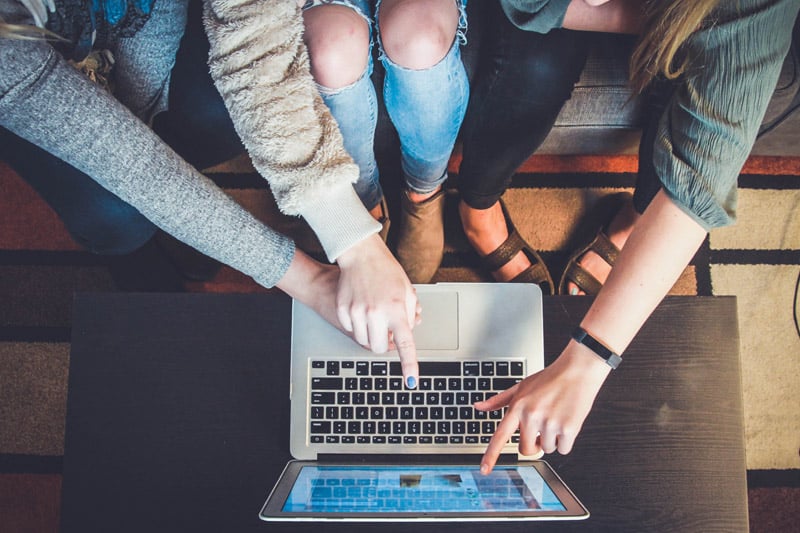 3 people sitting around a laptop and pointing at the screen