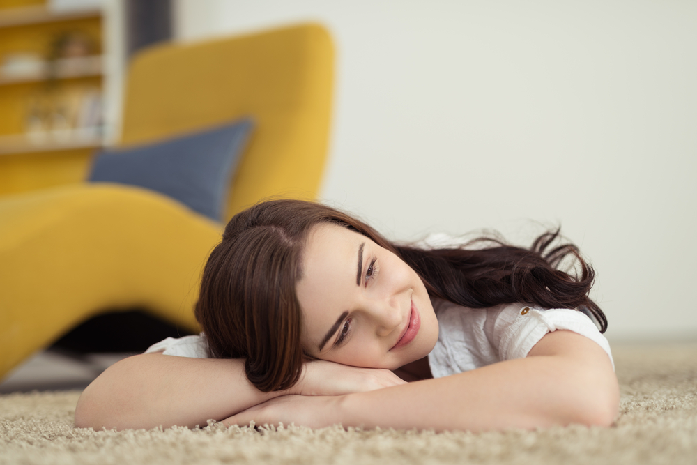 Happy woman lying on the carpet daydreaming with her head resting on her folded arms and a smile of pleasure on her face