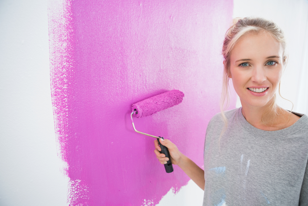 Pretty blonde painting her wall pink and smiling at camera in new home