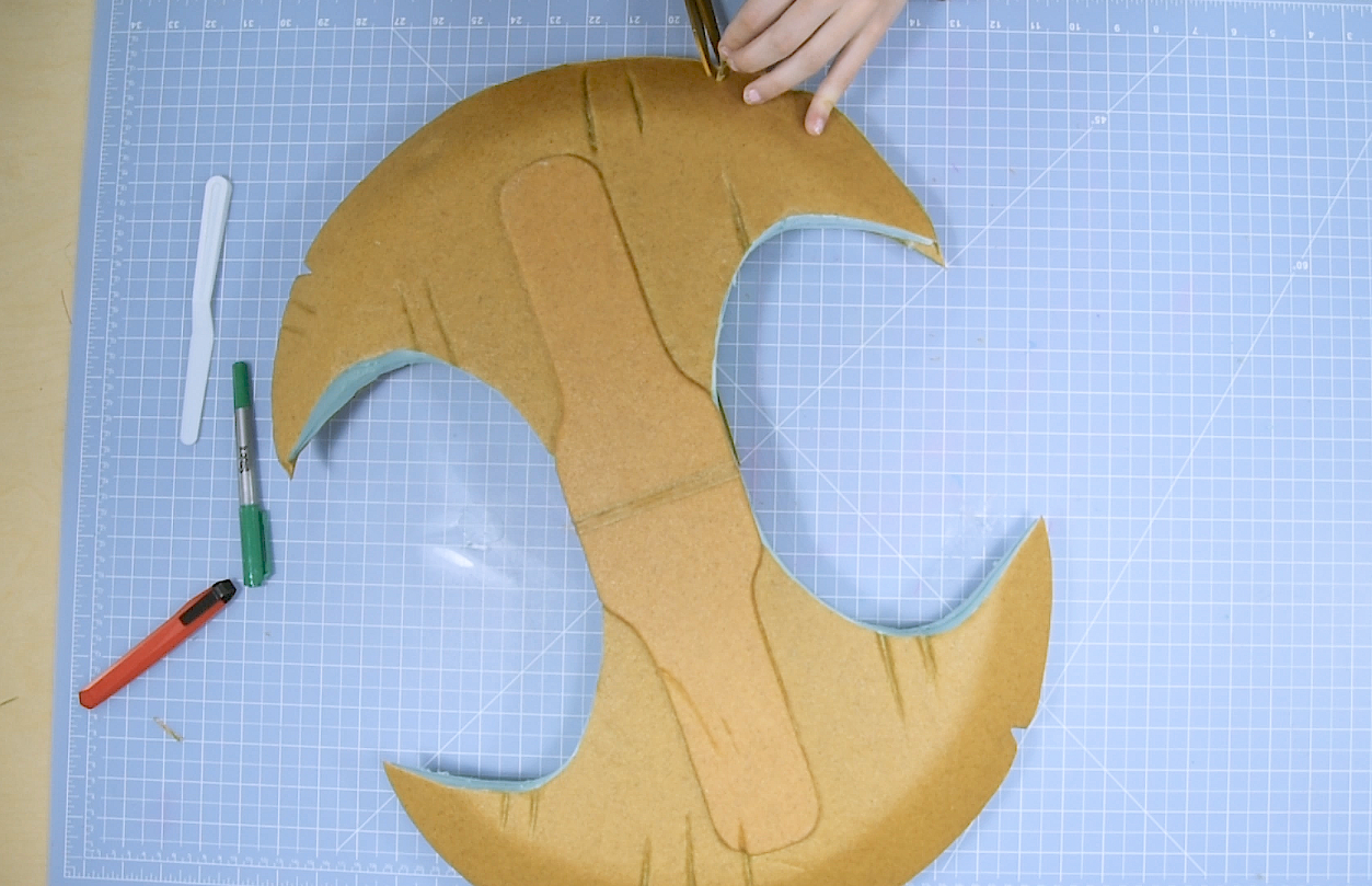 Cosplayer covering foam axe weapon with Worbla using scissors clay tools and heat gun