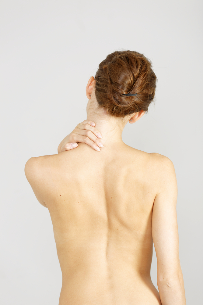 Young woman facing away massaging her neck from an ache or pain