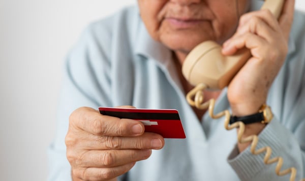 A senior reads their credit card number into a phone.
