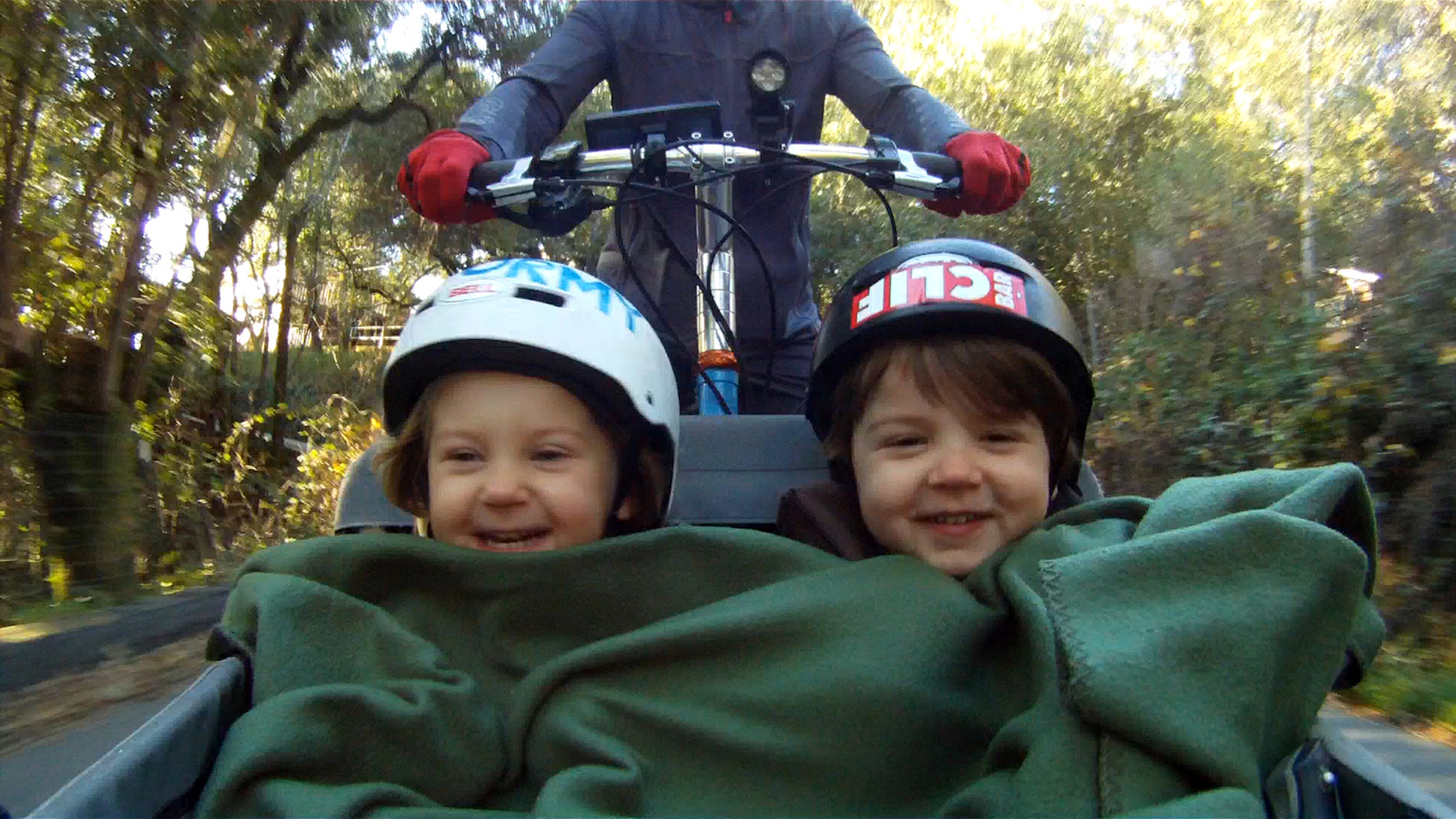 Two children laugh as they sit in the front of a cargo bike.