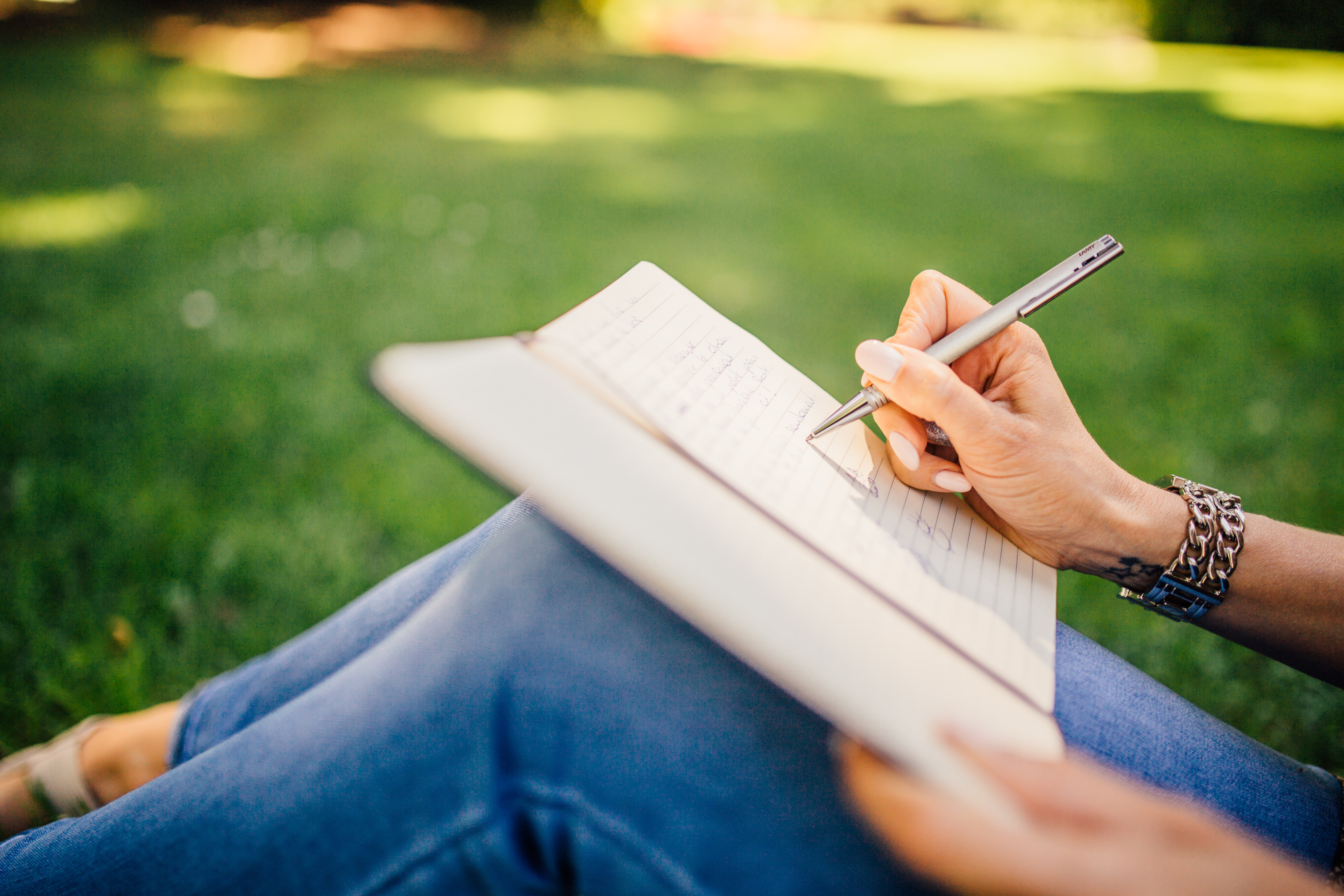 photo of a woman's hand writing in a journal in a park - 7 ways to explain anxiety to a partner - genomind