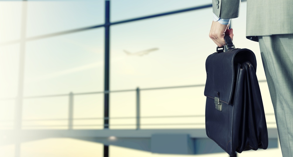 Back view of businessman at airport with suitcase in hand.jpeg