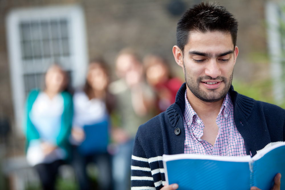 Student with a notebook outdoors with a group of people at the background